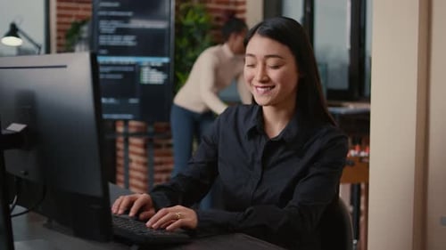 Asian Software Developer Smiling and Resuming Work Typing Code on Computer Keyboard