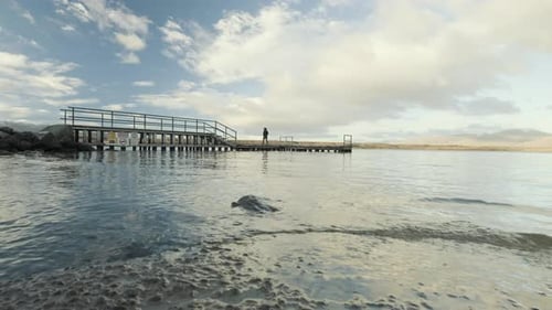 Tiefwinkelaufnahme eines Mädchens, das an einem sonnigen Tag alleine an einem Steg an einem See entlang geht