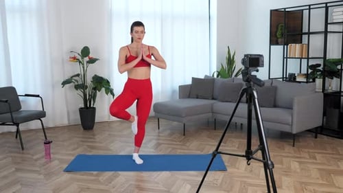 Blogger, instrutora de fitness feminina em forma, medita em pé sobre um tapete de ioga em casa