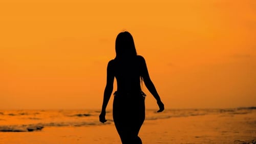 Silhouette einer Frau, die bei Sonnenuntergang am goldenen Strand entlang läuft