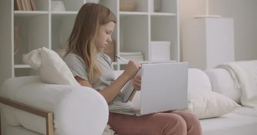 Teen Girl sieht Online-Training per Laptop von zu Hause aus an und lernt aus der Ferne, schreibt Notizen