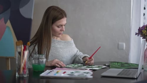 Young Woman Painting Green Leaves Indoors at Desk