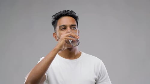 Glücklicher junger indischer Mann trinkt Wasser aus Glas 37