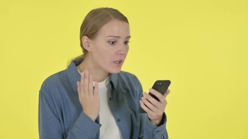 Surprised Woman Looking at Smartphone on Yellow Background