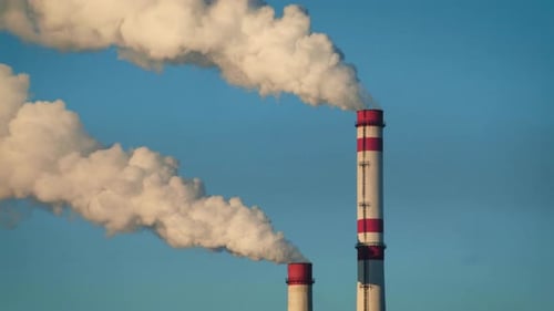Zwei Schornsteine blasen Rauch gegen einen blauen Himmel