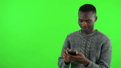Ein junger schwarzer Mann arbeitet mit einem Lächeln auf einem Smartphone - Green Screen Studio