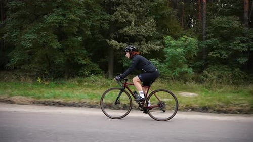 Professional Woman Biker Training in Forest Riding Uphill on Bicycle Preparing for Competitions