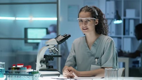 Young Adult Woman Sitting at Laboratory Desk with Microscope