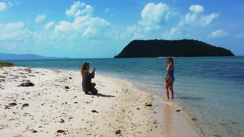 Tourist women taking pictures on shore of tropical island with sandy exotic beach and blue shallow t