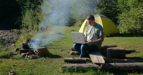A Man Works on a Laptop in a Tourist Camp in a Beautiful Forest