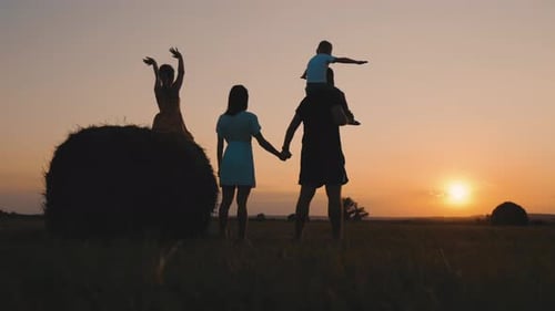 Silhouetted Family Enjoys Sunset on Rural Hay Field