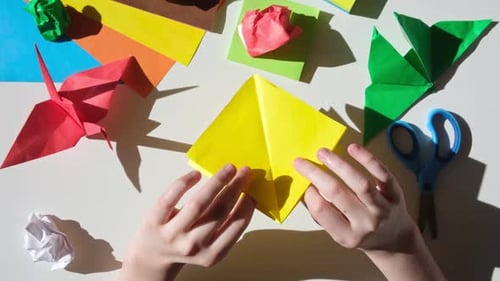 Hands Making Colorful Origami Figure on White Table
