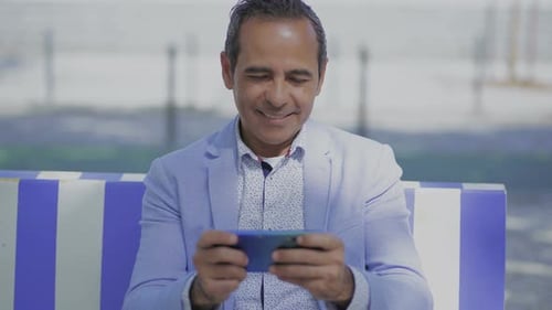 Man Sits on Bench Using Smartphone Smiling