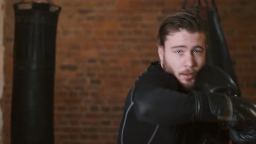 Dedicated Young Man Punching Boxing Bag at Gym