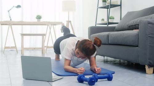 Una jovencita hace ejercicio y usa el ordenador portátil para ver un vídeo tutorial de yoga en casa.