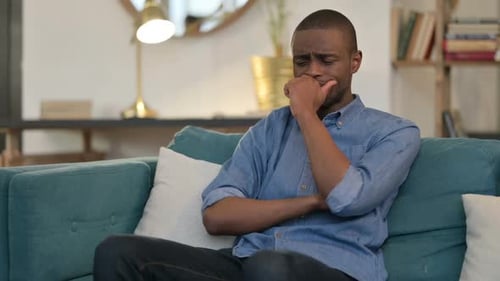 Young African Man Sitting and Crying on Sofa