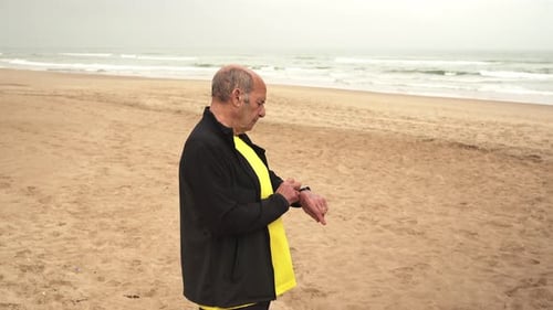 Aged sportsman checking smart watch on beach