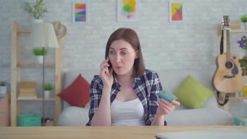 Woman on Phone Holding Credit Card in Home