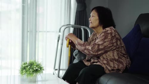 Senior Woman Sitting with Walking Stick at Home