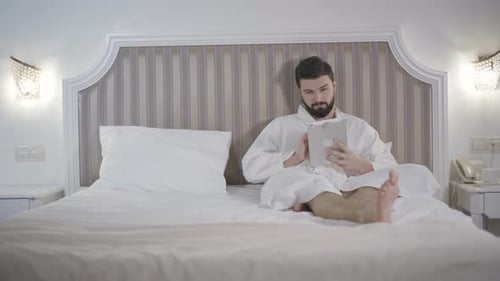 Man in Robe Uses Tablet on Bed