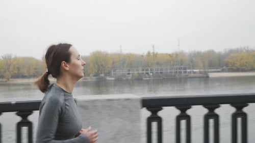 Woman Jogging Across Bridge on Overcast Day