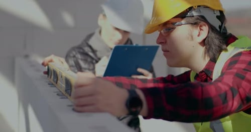 Male Worker Examining Wall with Level By Female Contractor
