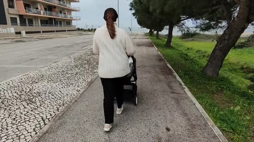 Back View Of A Mother Walking Outdoors With Son In A Baby Stroller. tracking shot