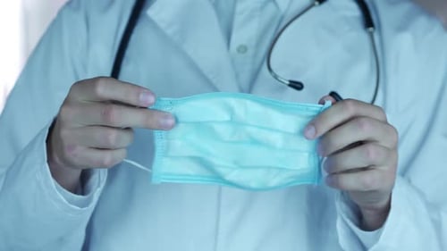 Doctor with Stethoscope Puts on a Surgical Mask