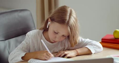 Close-up Child Learns Writes in Notebook Listening in Headphones Teacher Looks at Laptop Screen