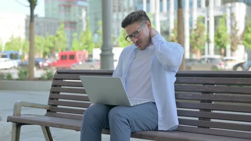 Man With Laptop Rubbing Neck on Bench