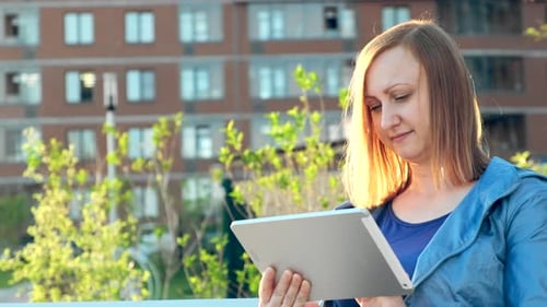 Woman Using Tablet Computer Sitting on Bench in City