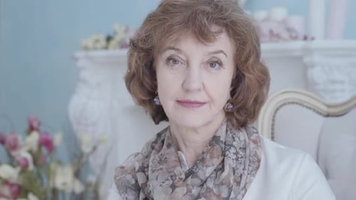 Happy Positive Elegant Mature Lady Sitting in the Armchair Looking in the Camera Close Up. Flowers