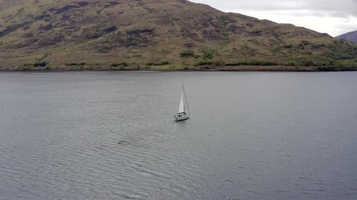 Eine Yacht, die Segel hebt, umgeben von Bergen und Wäldern in einem See