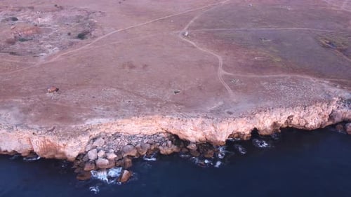 Top down aerial view of waves splash against rocky seashore, background. Flight over high cliffs of