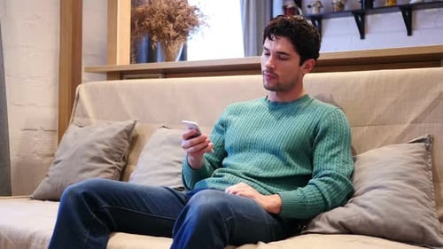 Young Adult Using Smartphone on Couch Indoors