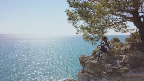 Aerial View of Young Man Traveler on Rock Cliff Against Sea.