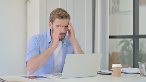 Man in Office With Headache Works on Laptop