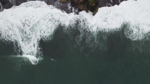 Top down aerial view of giant ocean waves crashing and foaming in coral beach