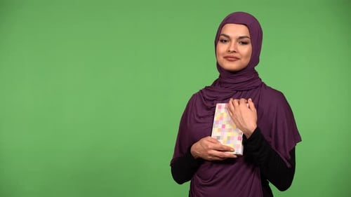 A Young Beautiful Muslim Woman Holds a Book in Her Arms and Smiles at the Camera Green Screen