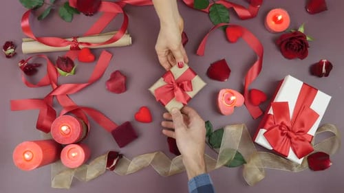 Male hand is giving wrapped gift box with tied red bow to female hand for St. Valentine's Day