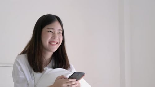 Smiling Young Adult Using Smartphone on Bed