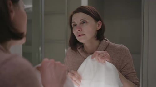 Woman Dries Face With Towel in Bathroom Mirror
