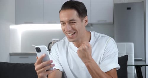 Man Reacts to Positive News on Phone Indoors