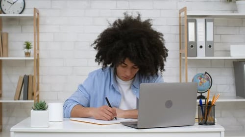 Afrikanischer Student lernt am Laptop und macht sich zu Hause Notizen