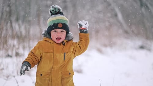 Glücklicher Kleinkind-Junge, der Spaß hat und Schneebälle auf Winterschneefall-Hintergrund spielt