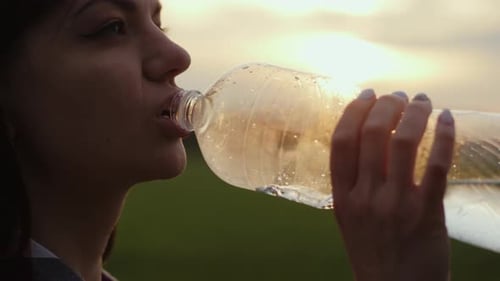 Woman Quenches Her Thirst in a Field at Sunset