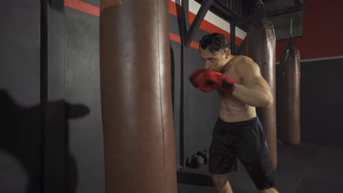 Strong caucasian man punching bag, combat punches in boxing sport club workout at training