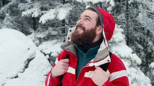 Footage of young bearded hiker man looking up at mountain cliff during snowing storm