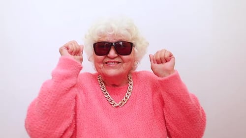 Portrait of Funny Amazed Surprised Senior Blonde Woman in Sun Glasses and Pink Sweater on White