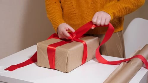 Woman Tying Red Ribbon on Wrapped Gift